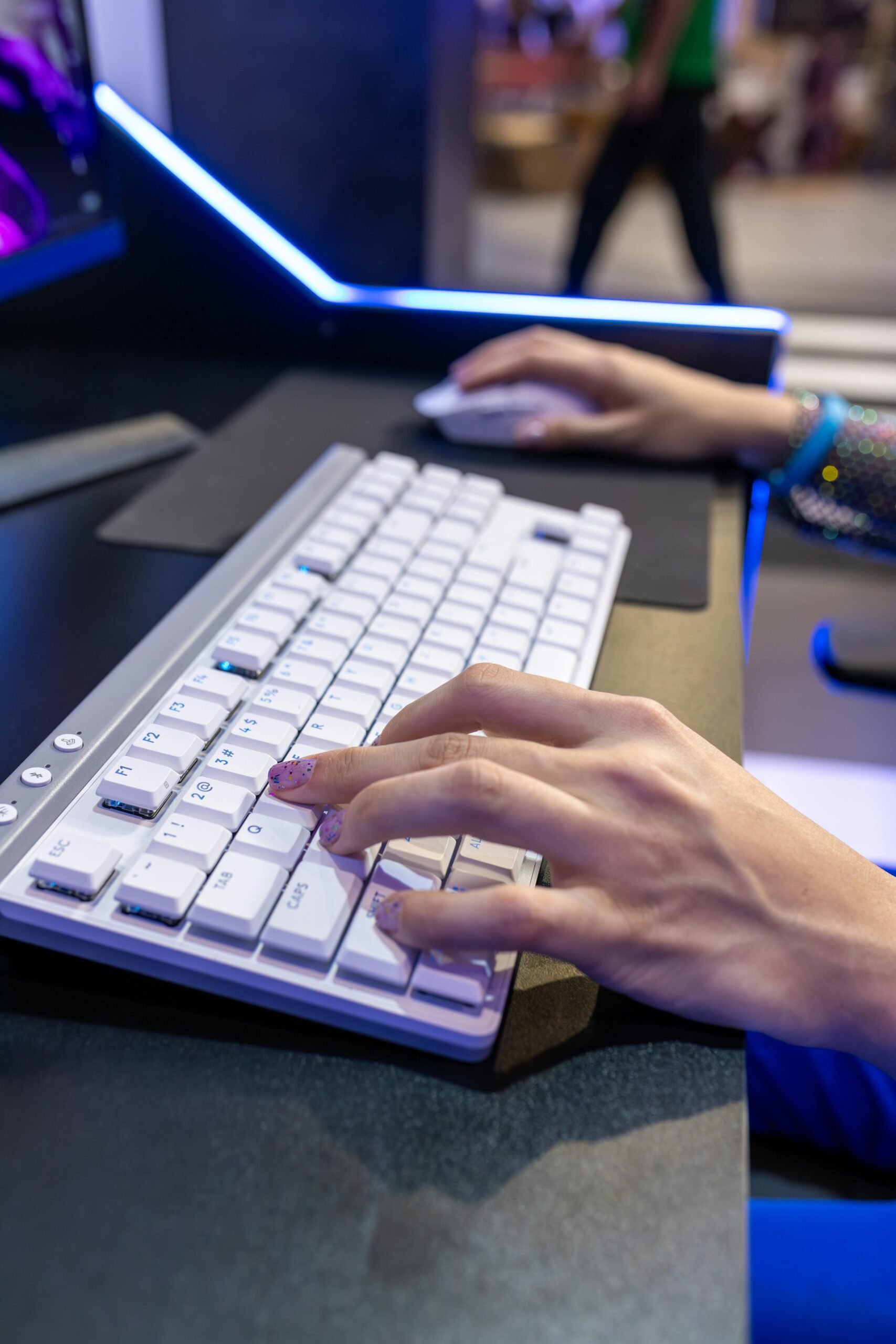 Hands typing on a white compact TKL mechanical keyboard with wrist rest and wireless mouse on an ergonomic desk setup